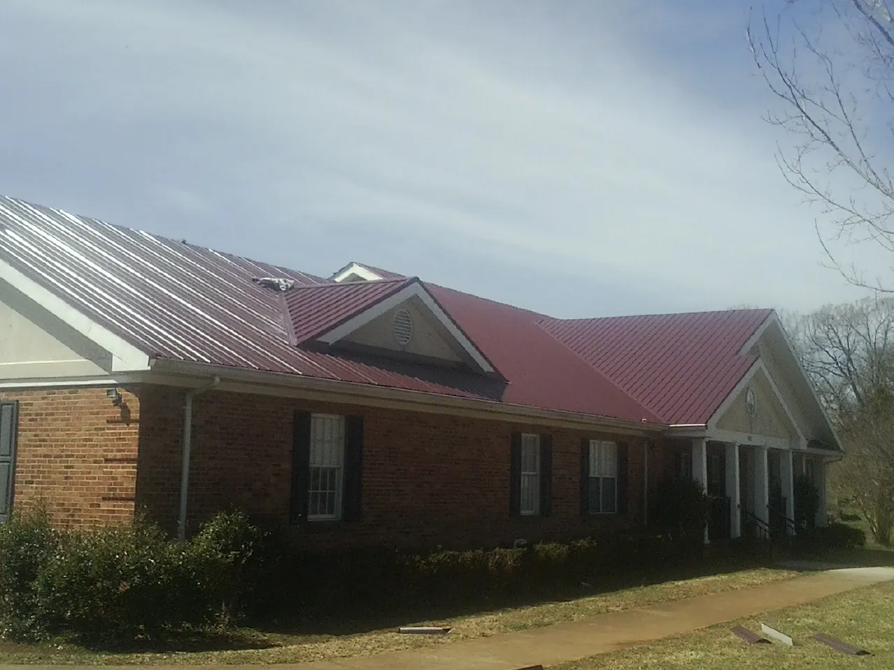 Red metal roof with gabled entries on a long brick building, from a Hail Damage Roof Repair job in Bush