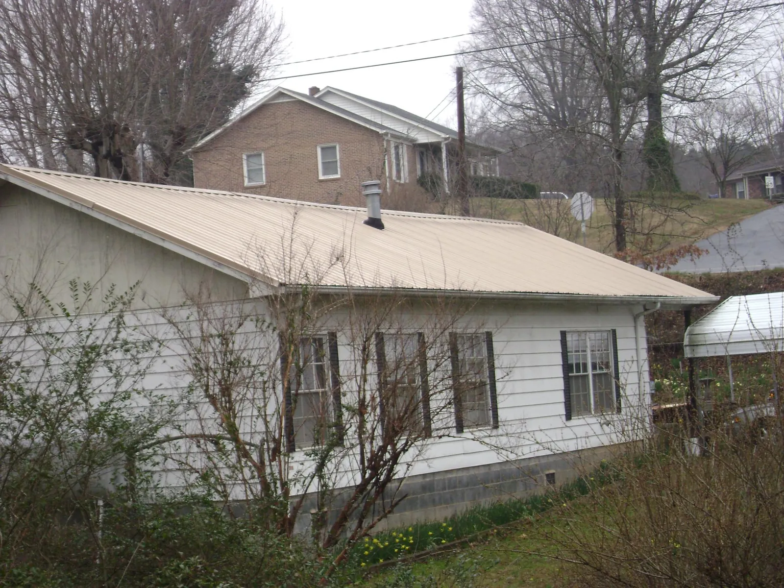 Tan metal roof on a white sided house set into a hillside — Commercial Roofing by Roofing Brothers in Bush